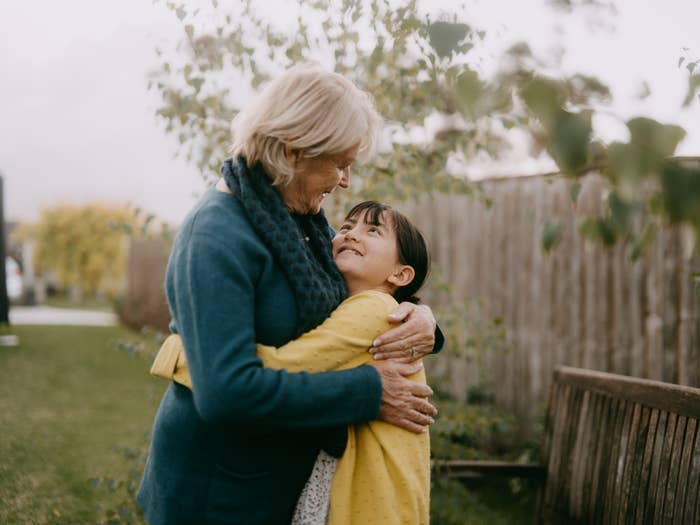 Grandmother and granddaughter share a warm embrace in a backyard, smiling and looking at each other lovingly