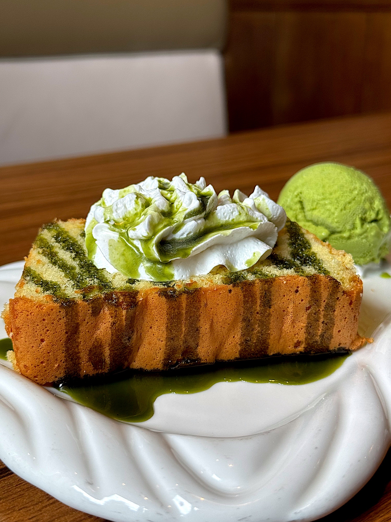 Cake slice with green matcha stripes, topped with whipped cream, served with a scoop of green ice cream on a white plate