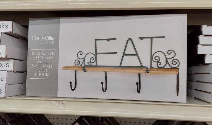 Wall shelf with "EAT" design, featuring 4 hooks, displayed in a store packaging