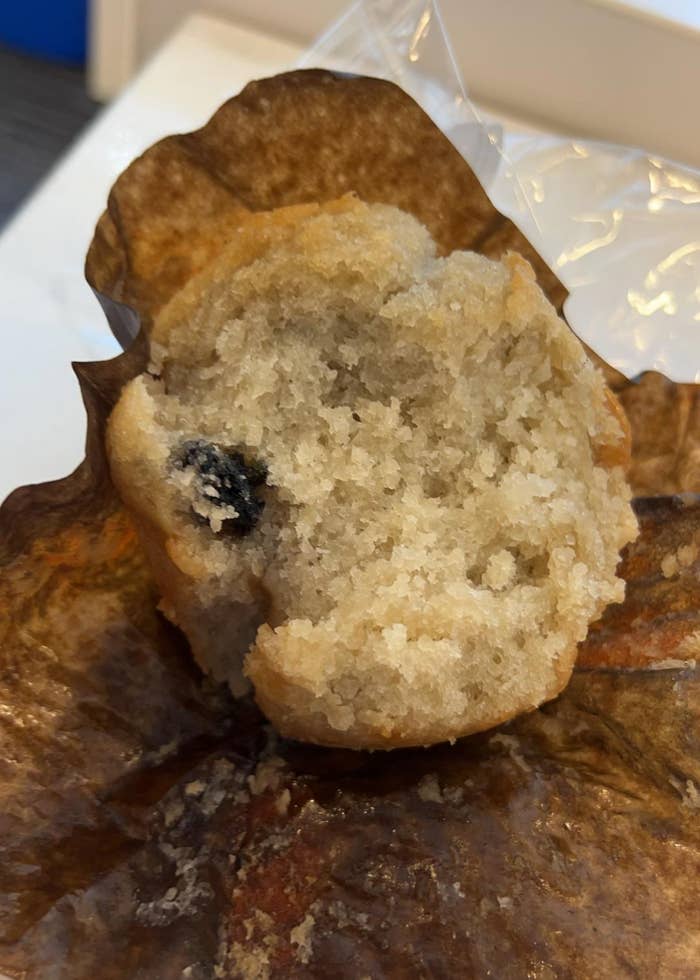 Partially eaten muffin with a single visible blueberry, resting on a brown paper wrapper