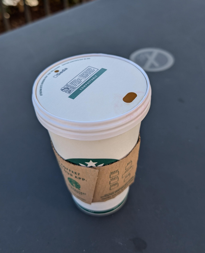 Coffee cup with a cardboard sleeve and a lid, placed on a table with a no-smoking sign