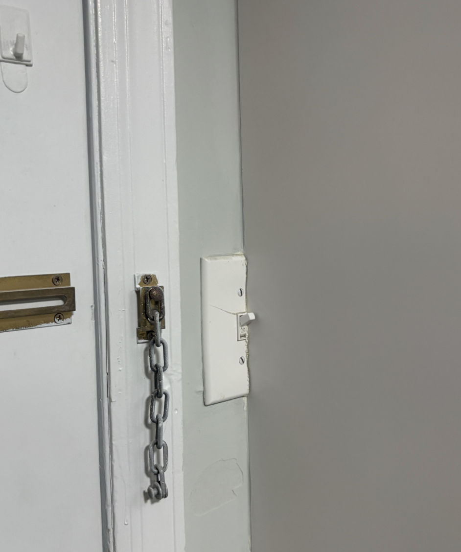 A door with a chain lock beside a light switch on the wall
