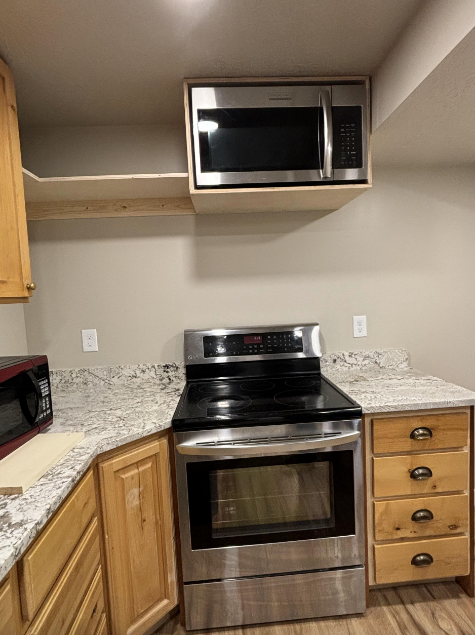 Kitchen with oven and countertop microwave below cabinets where another microwave is placed, showcasing an unusual kitchen design