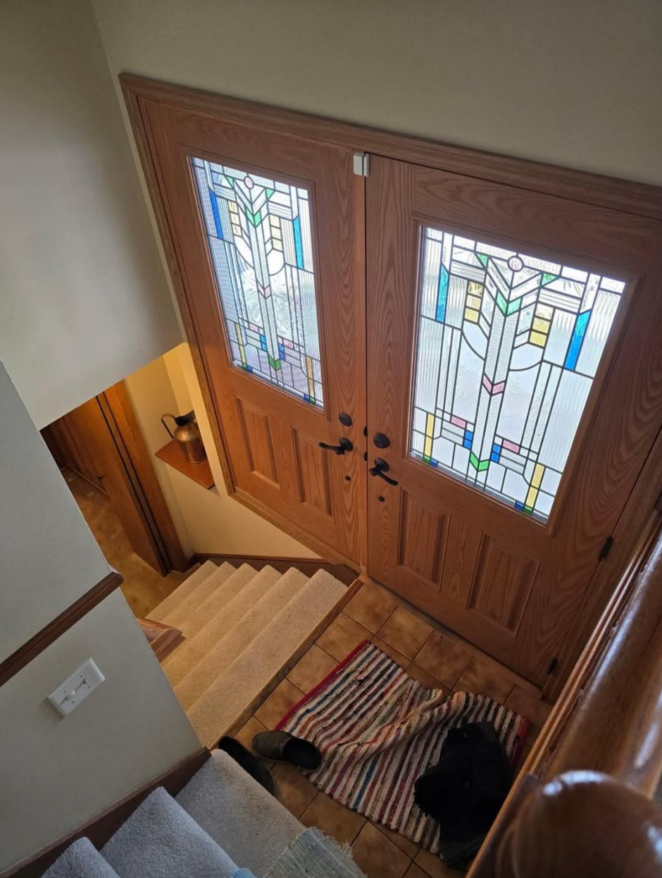 View from stairs of an entryway with stained glass double doors, a striped mat, shoes, and a bag on the floor