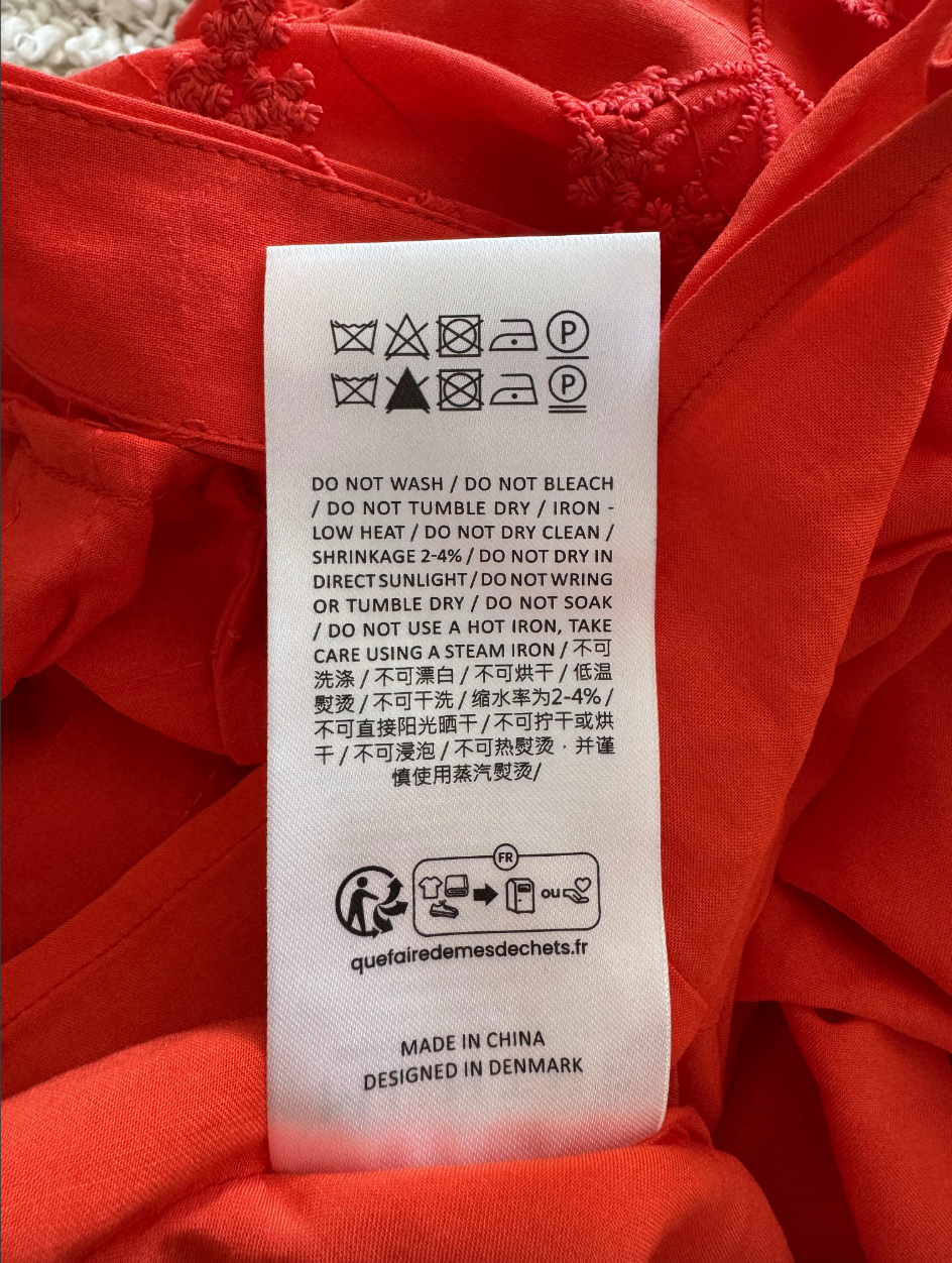Clothing care label with instructions on washing, drying, and ironing to prevent shrinkage; includes a website and manufacturing details