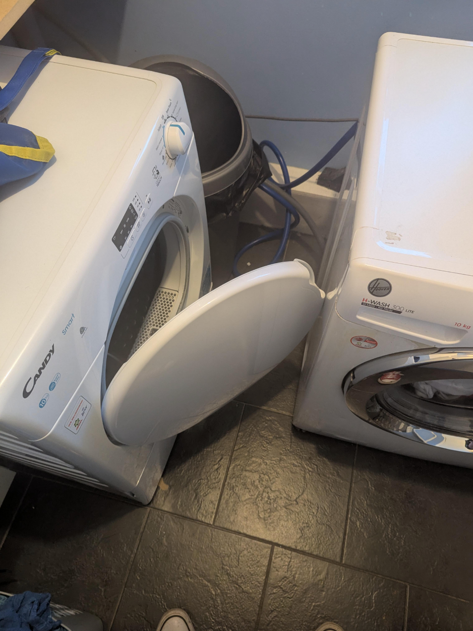 Two white front-loading washing machines are placed side by side in a laundry room, with one door open, showing a small space between them