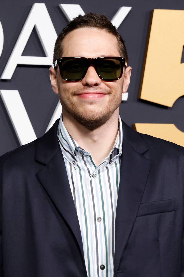 Pete Davidson in sunglasses wearing a striped shirt and dark blazer at an event