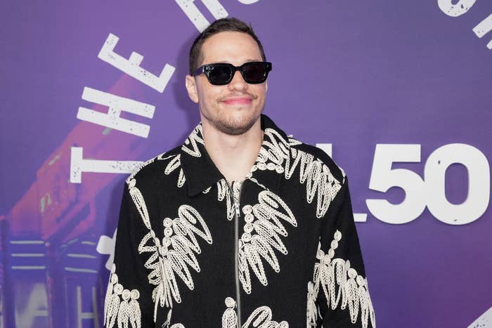 Pete Davidson in patterned jacket and sunglasses smiles at an event