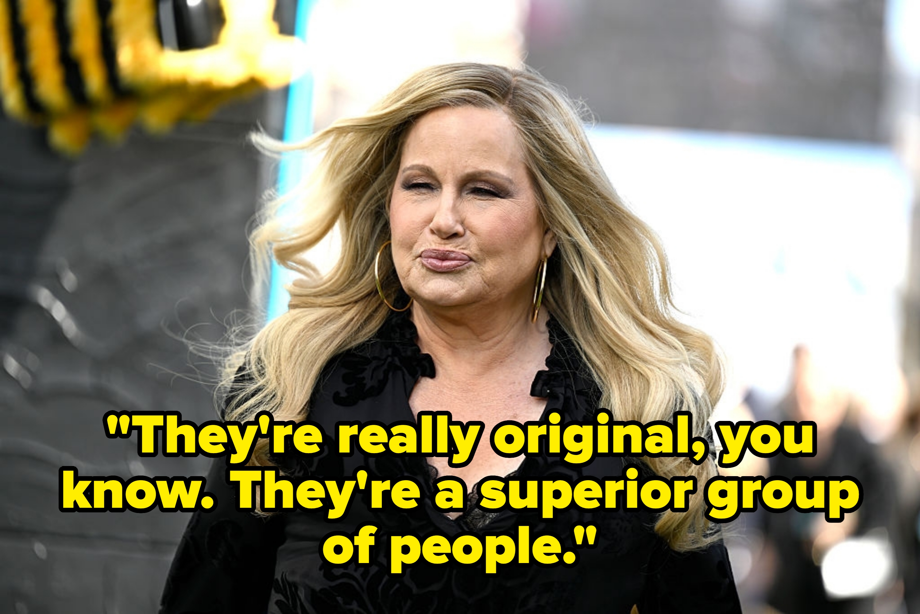 Person in a black, long-sleeved top with lace detail and hoop earrings, outdoors. They are walking and have long, flowing hair