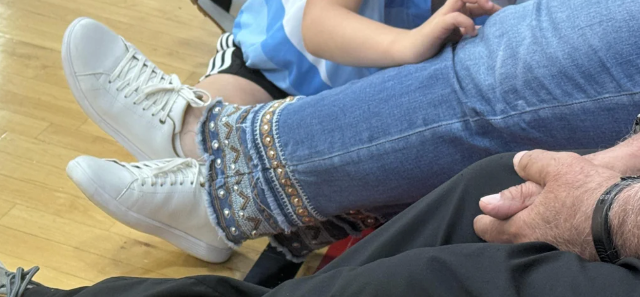 Person sitting with crossed legs, wearing bejeweled socks over jeans and white sneakers, next to a child in casual sports attire