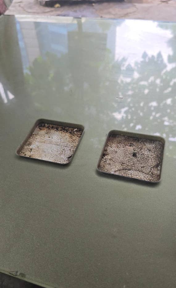 Square indents on a surface, possibly for small planters, showing cracked and dried soil inside