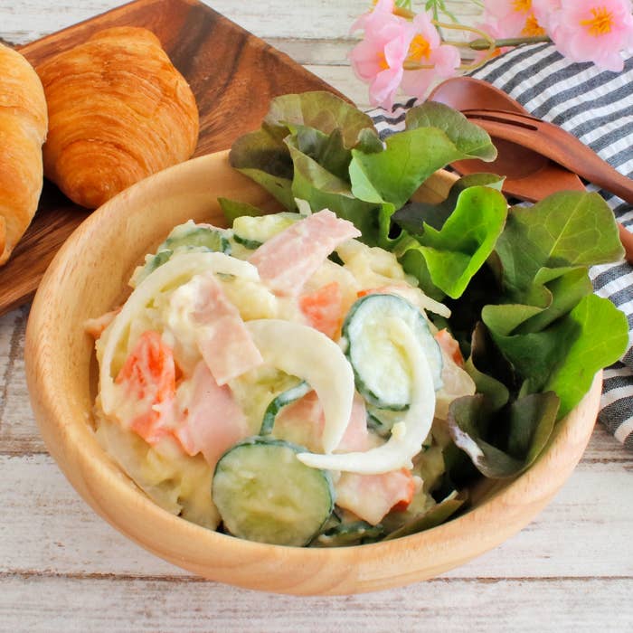 クロワッサンとサラダが木のボウルに盛られたテーブルセッティング。サラダにはキュウリ、タマネギ、ハムが含まれている。