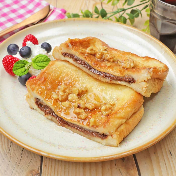 フレンチトーストにくるみとシロップをトッピングした朝食プレート。側面にベリーとミントの飾り。