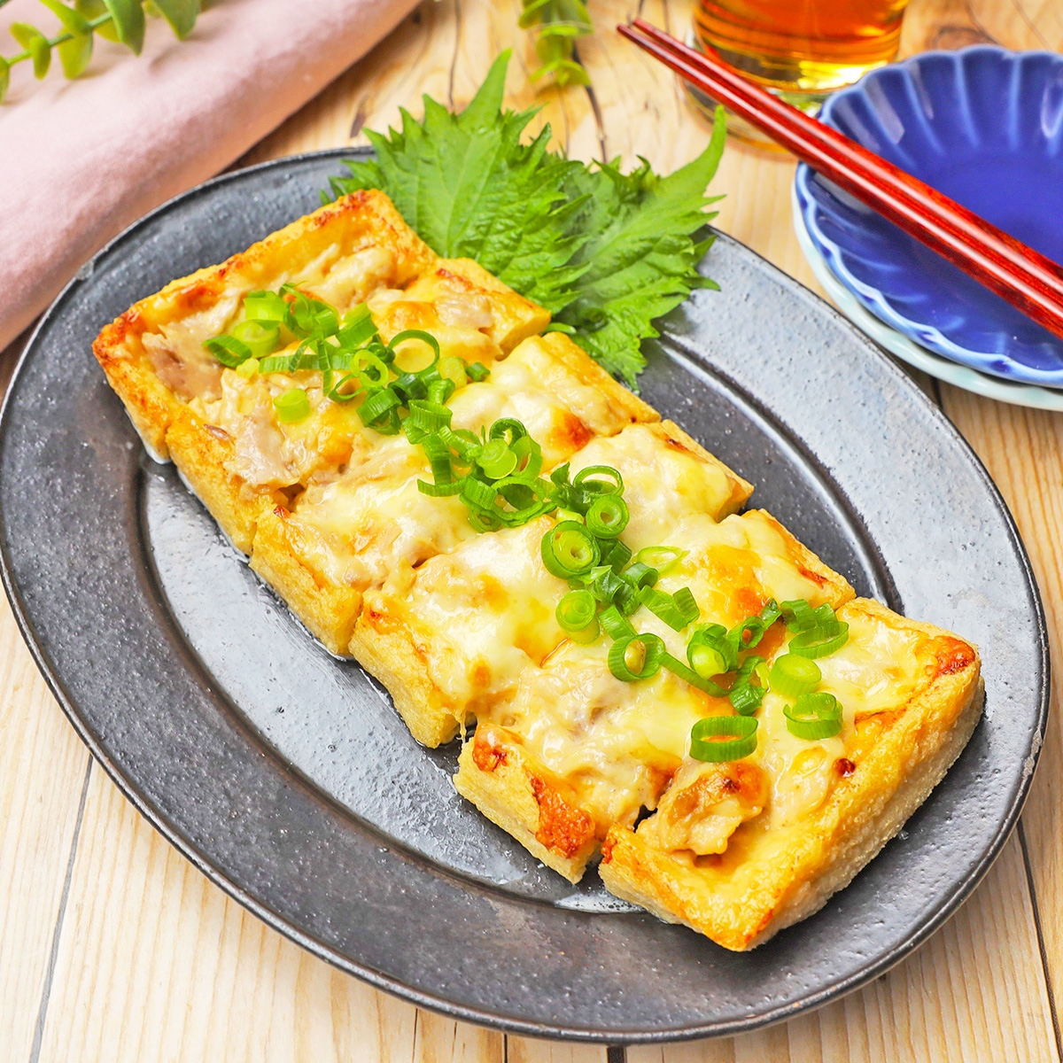 厚揚げの上にチーズとネギがトッピングされた料理が皿に盛られている。箸と飲み物が添えられている。