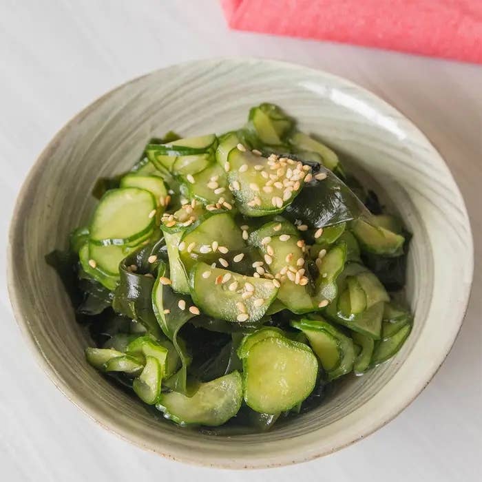 陶器のボウルに盛られたキュウリと海藻のサラダ、ゴマがトッピングされています。