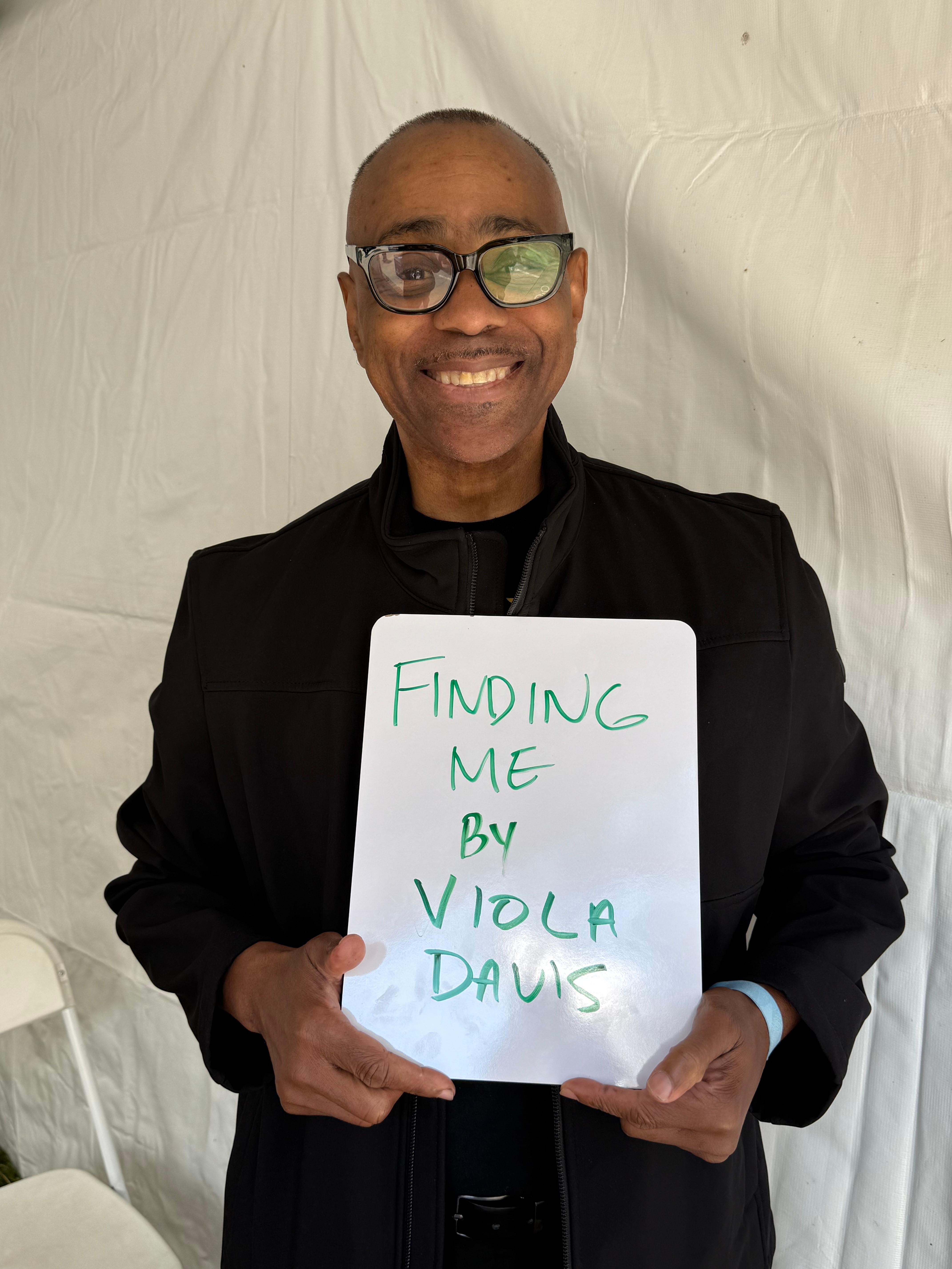 Man smiling, holding a whiteboard with "Finding Me by Viola Davis" written on it