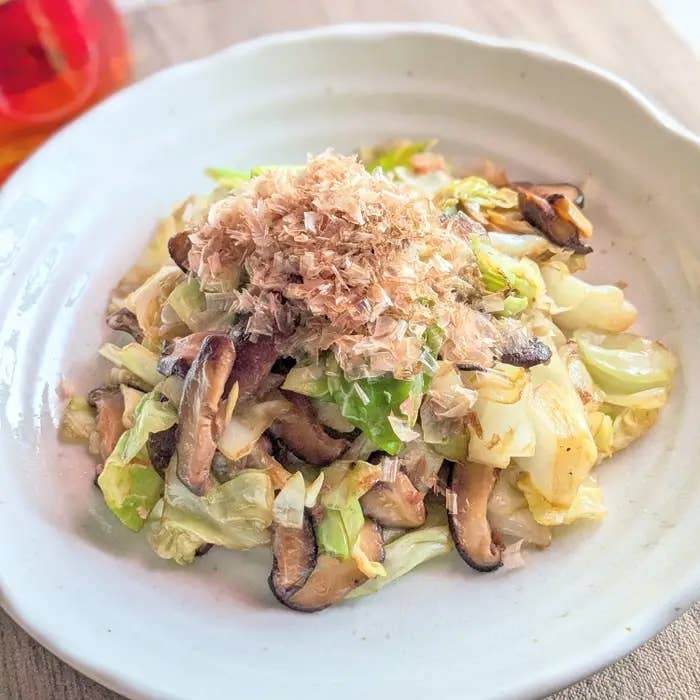 キャベツとしいたけの炒め物が白い皿に盛られている。上にはかつお節が載っている。