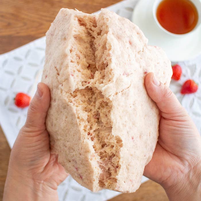 人が生地を割っているシーン。後ろにティーカップとイチゴが置かれている。