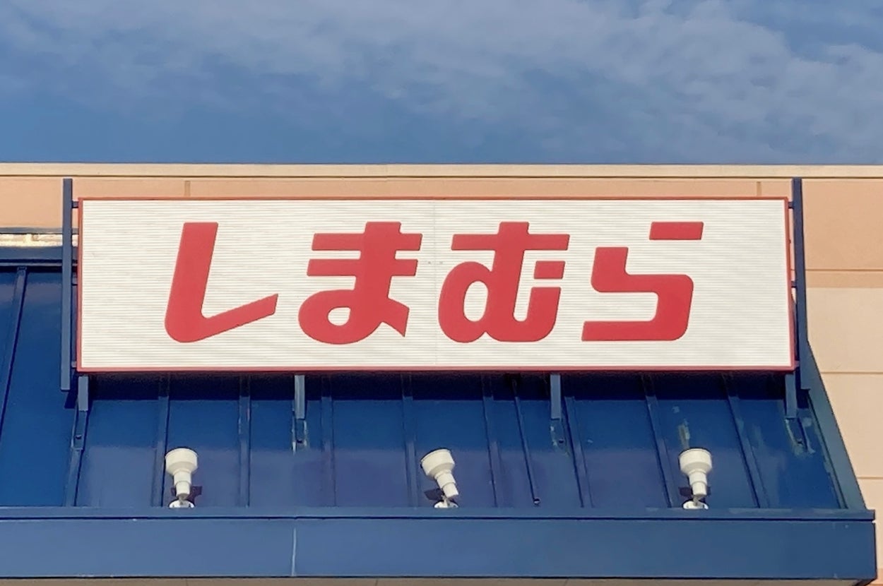 A storefront sign in Japanese text, "しまむら," above a blue awning