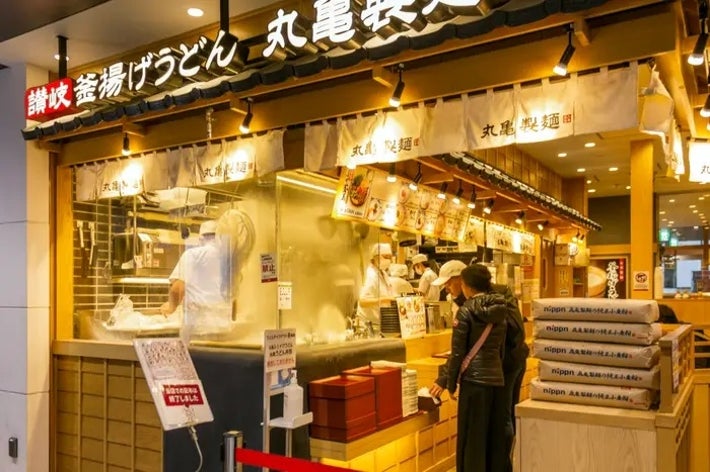人々がうどんを注文している丸亀製麺の店頭。スタッフが調理中。