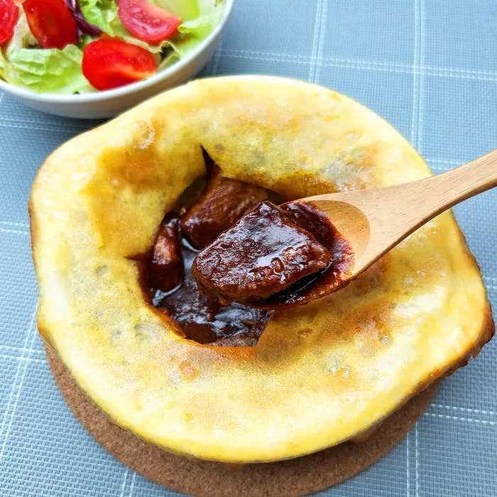 サラダを添えた焼きカレーパイがテーブルに置かれている。スプーンがカレーをすくっている。