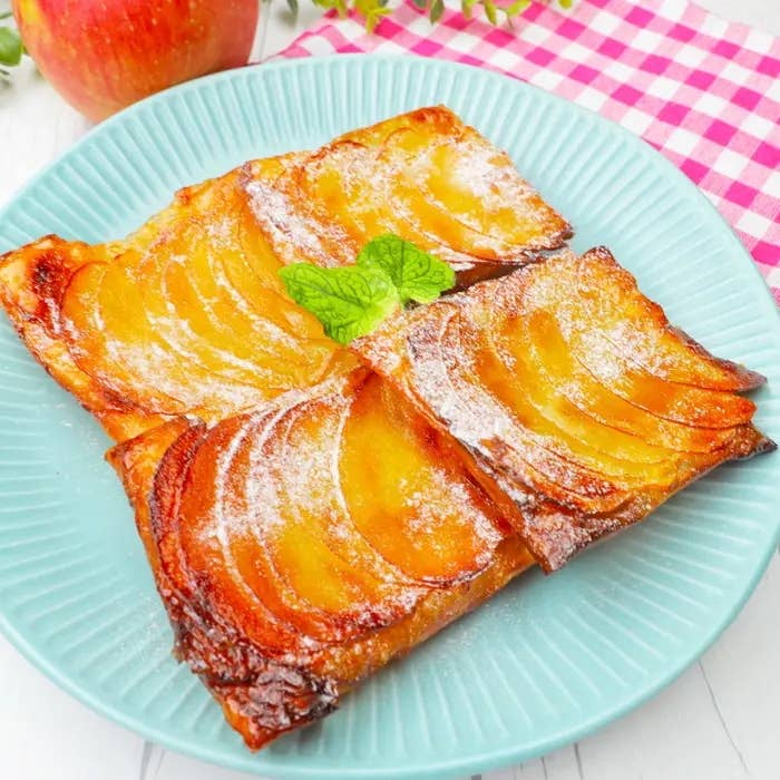 リンゴの薄切りを乗せたタルト、焼き色がついて美味しそうに見える。中央にミントが飾られている。