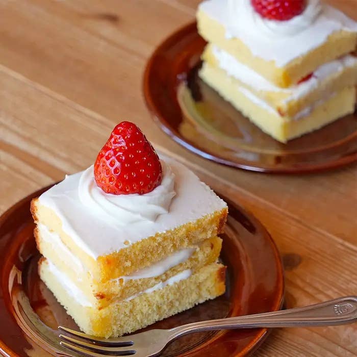 いちごが添えられた層になったケーキが2つ、茶色の皿に盛られている。食卓にフォークが置かれている。