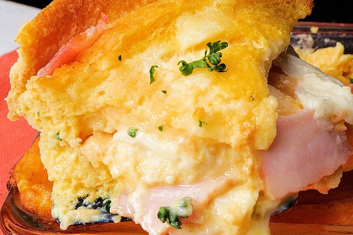 厚切りのハムとチーズが重なった焼きカサロールの一部を持ち上げている様子。クリーミーでボリューム感がある。
