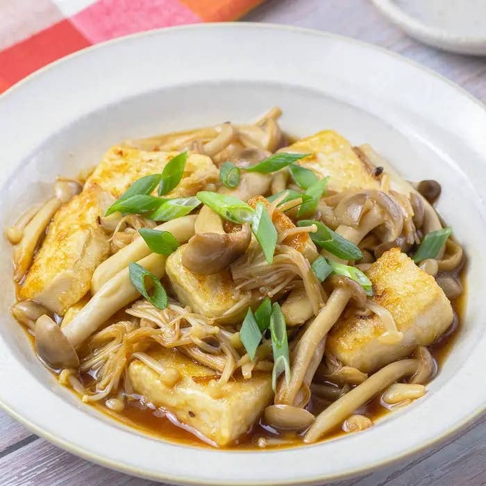 豆腐ときのこの炒め物が白い皿に盛られている。小ねぎが上にトッピングされている。