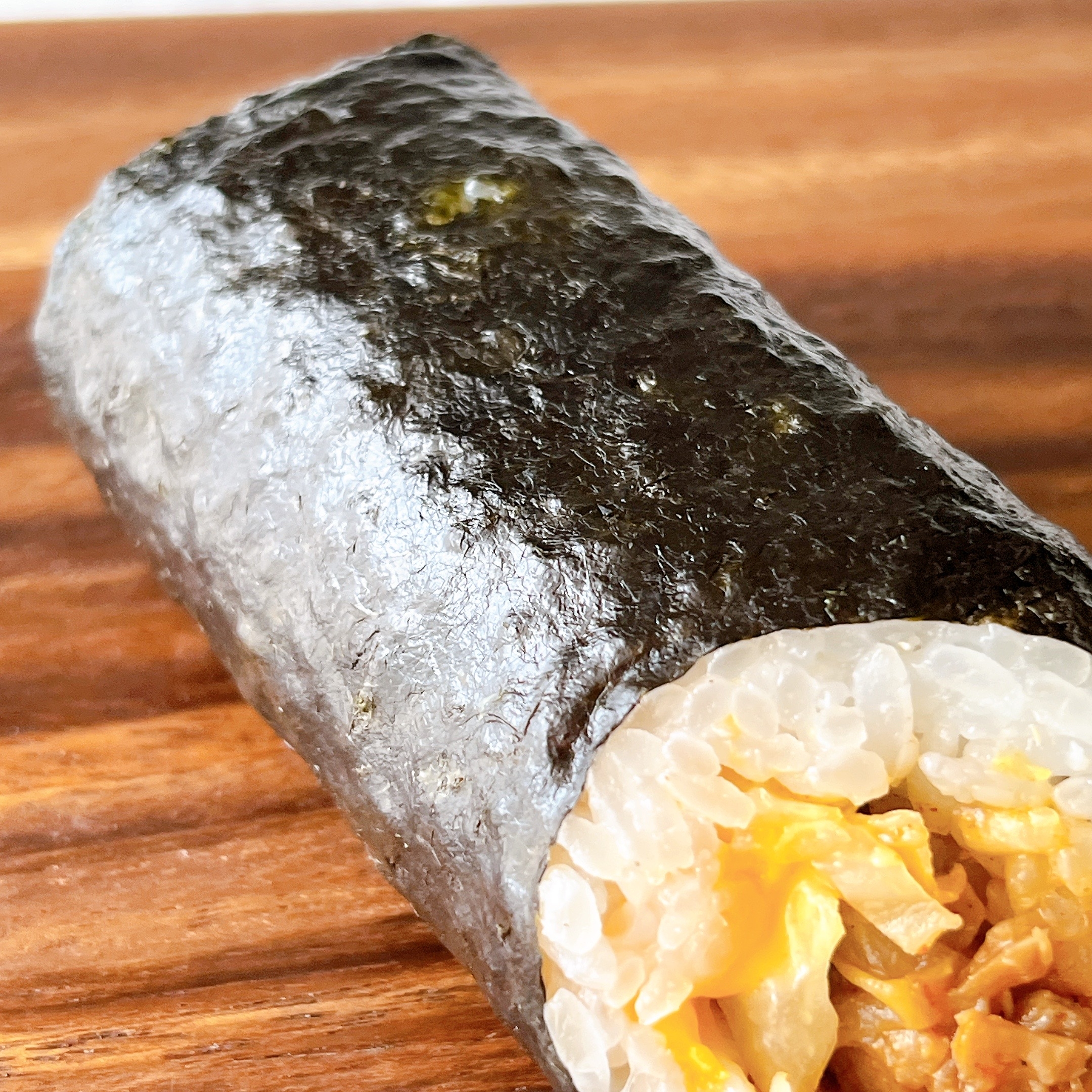 海苔で包んだおにぎり。中には具材が見える。木の台にのせられている。