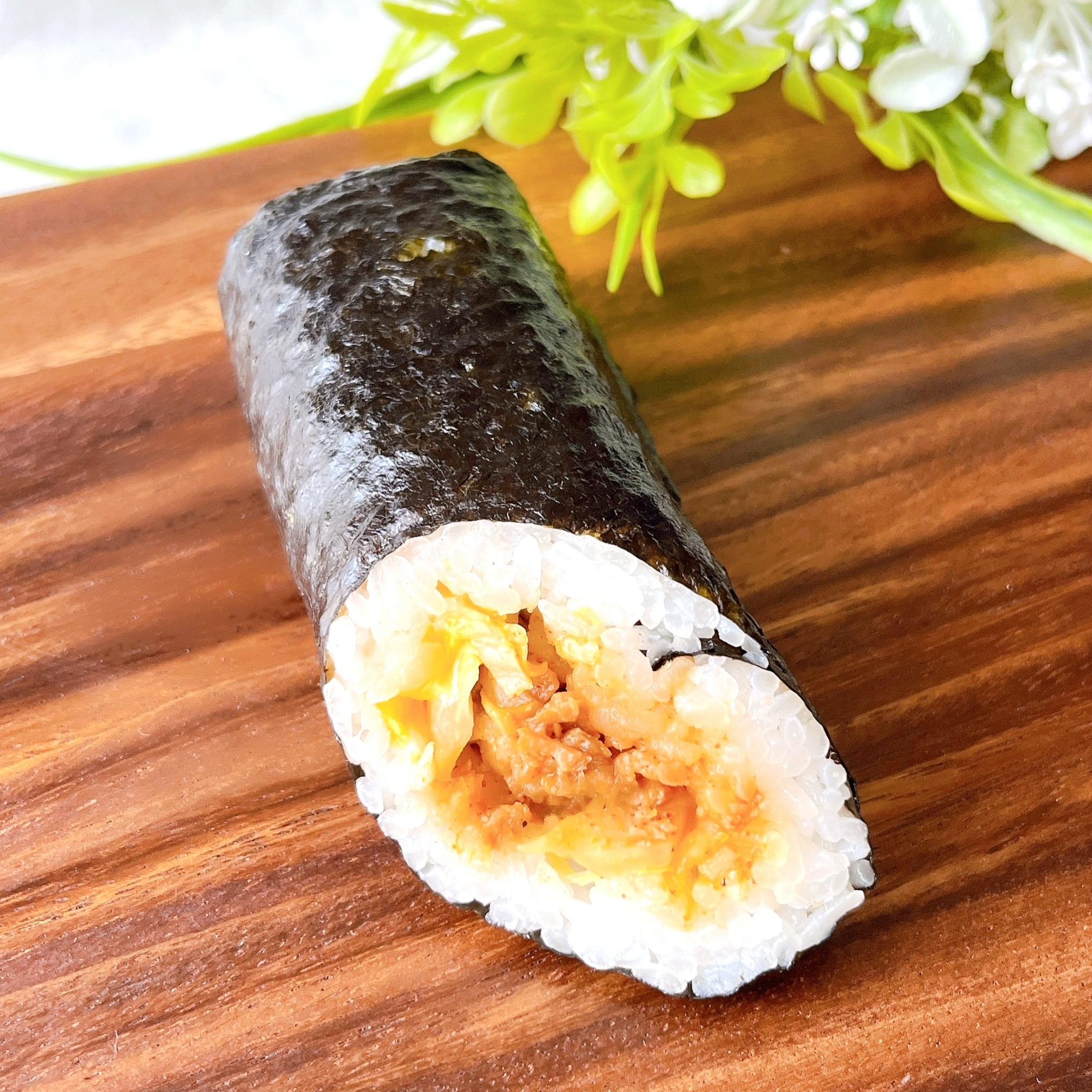 寿司ロールが木の板の上に置かれている。背景に緑の植物。