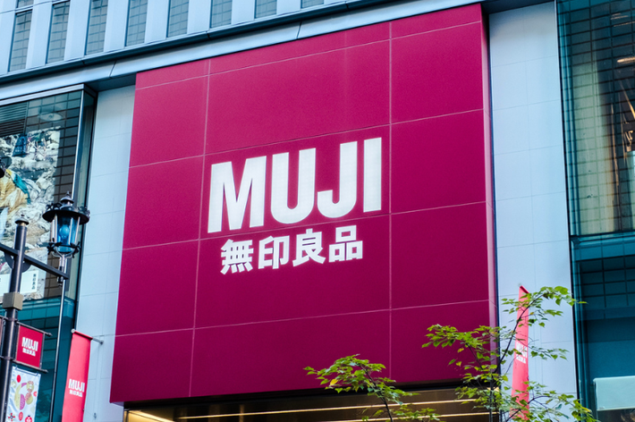 MUJIストアの外観。大きな看板には「MUJI 無印良品」のロゴが表示されています。商業施設の入り口が見えます。