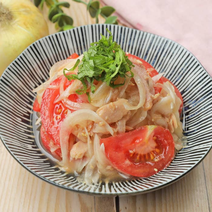 トマト、玉ねぎ、鶏肉が盛られたお皿のサラダ料理。シソの葉がトッピングされています。