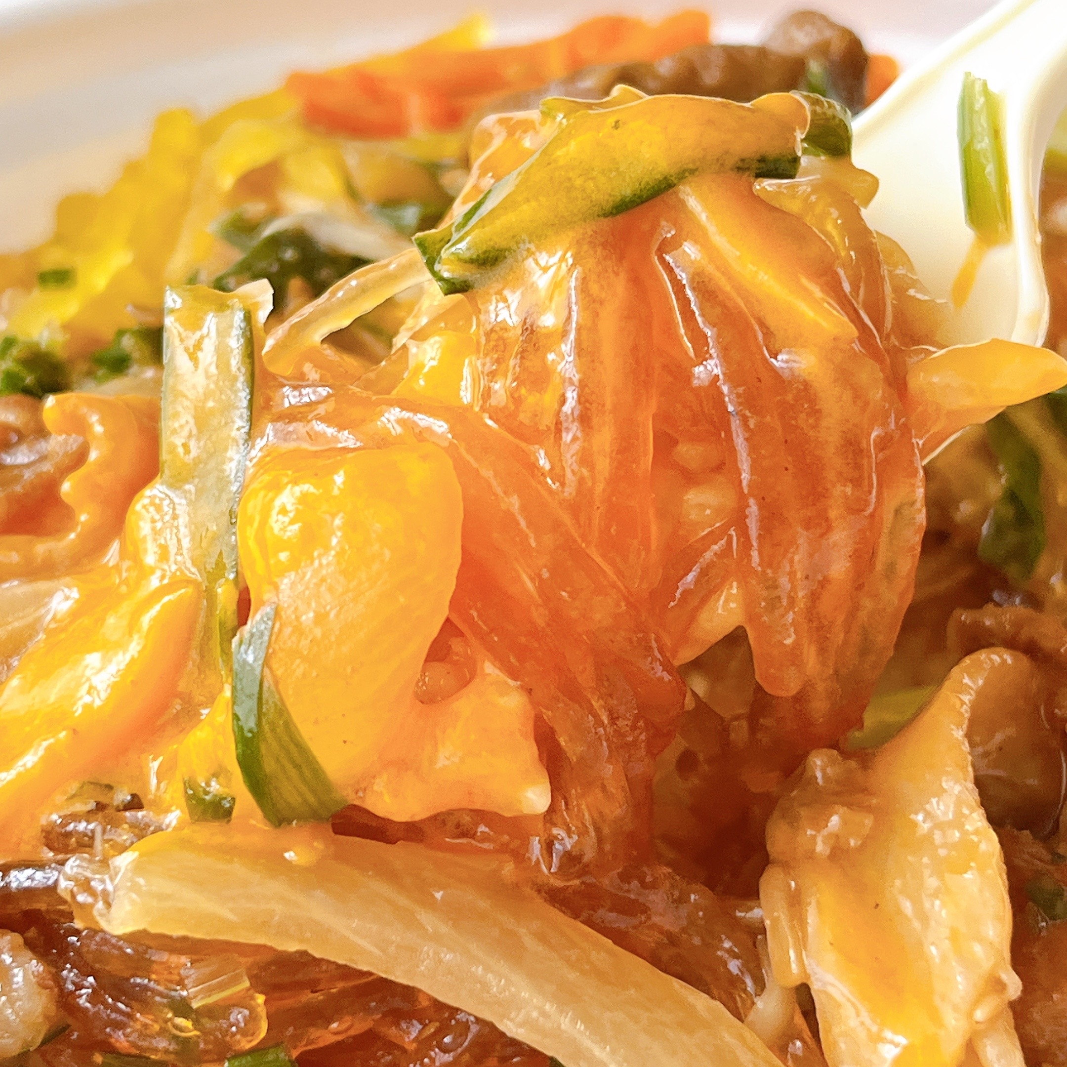 おいしそうなチャプチェがフォークに巻かれている。春雨、野菜、肉が絡んでいる。