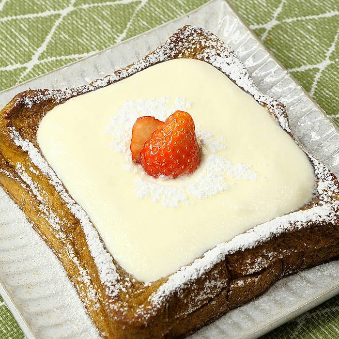 デザート皿に乗ったトーストの上にクリームとイチゴが盛られている。