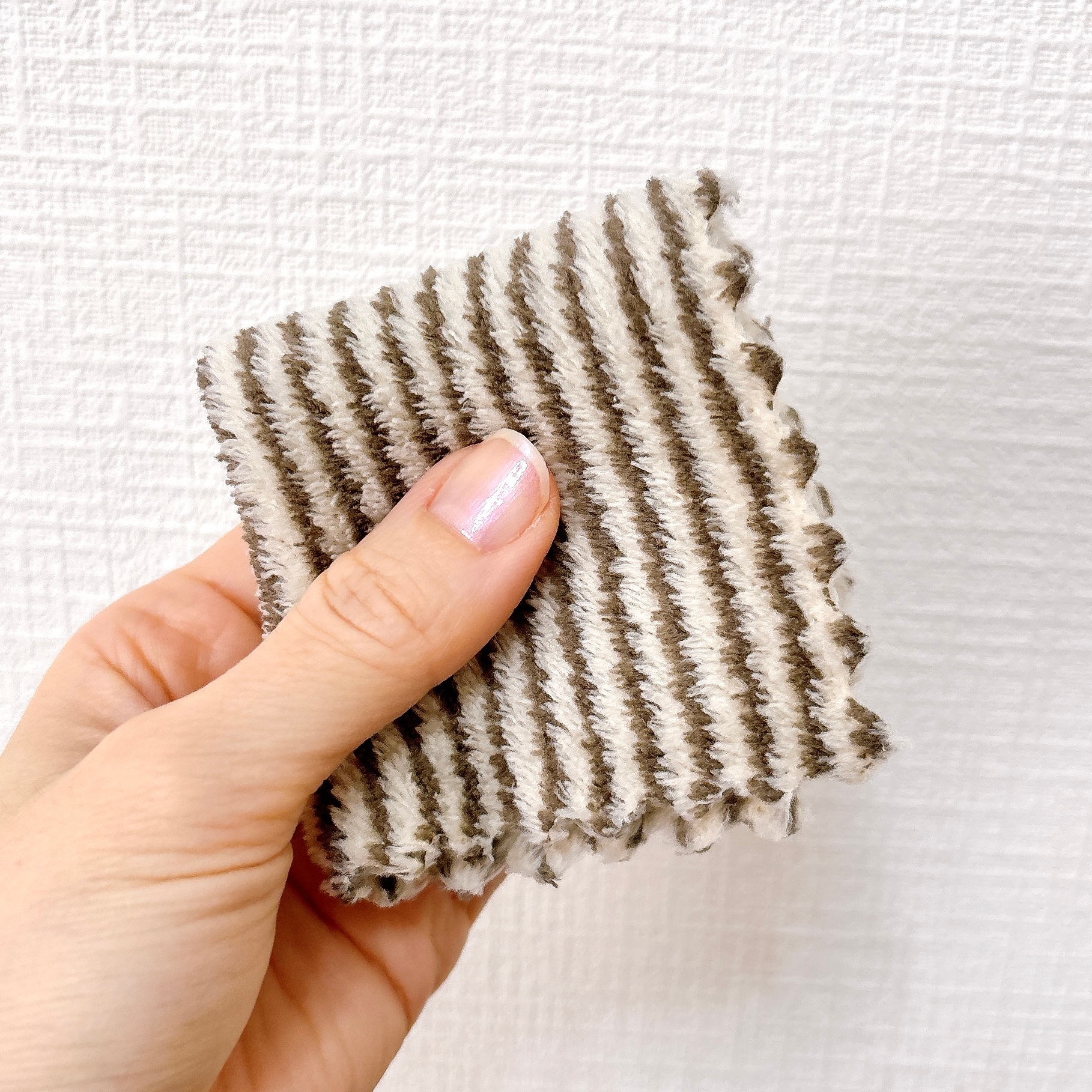 手に持たれた縞模様の布サンプル。背景は質感のある壁。