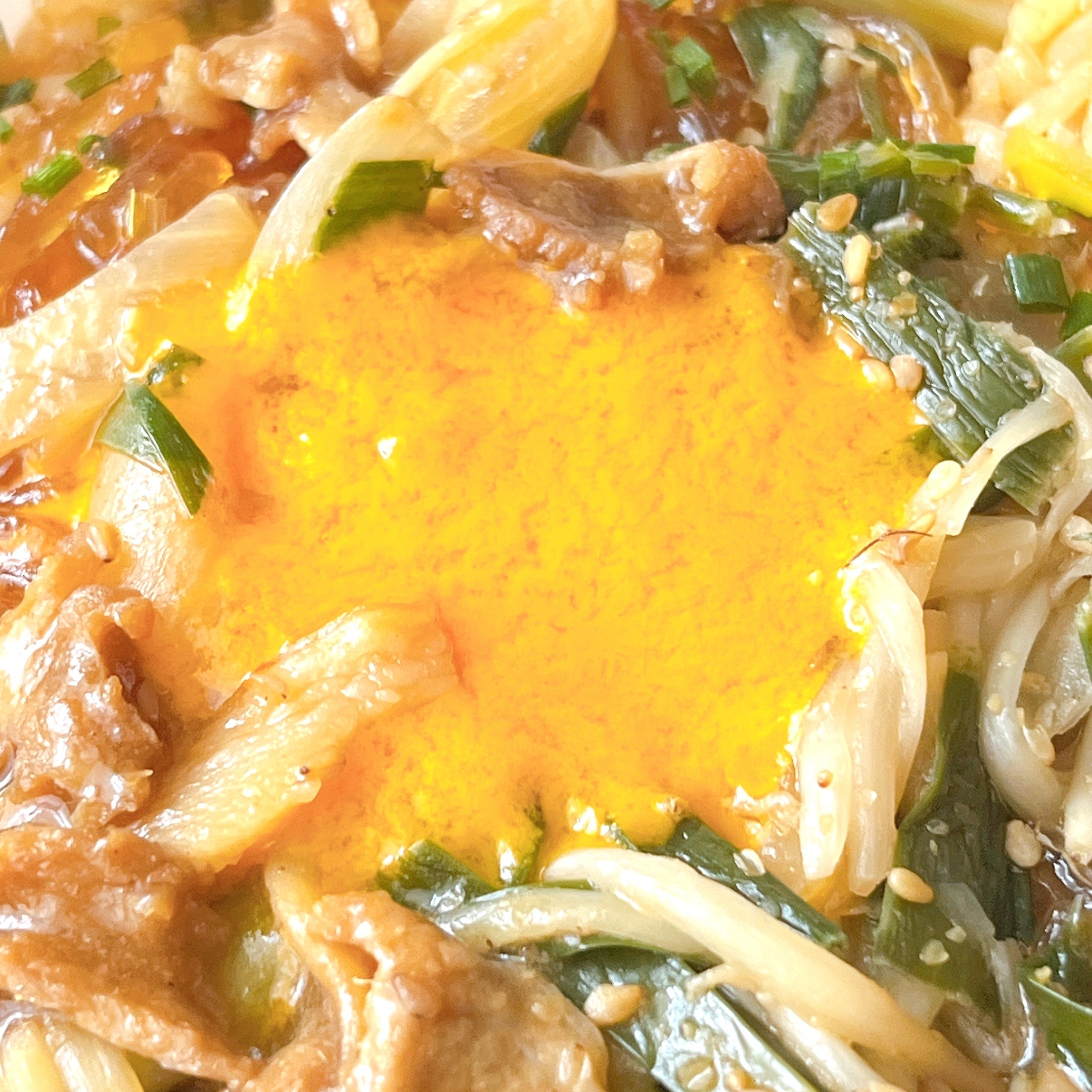 韓国料理のビビンバ。中央に生卵の黄身が載っており、周囲には肉、野菜、ゴマが盛り付けられている。