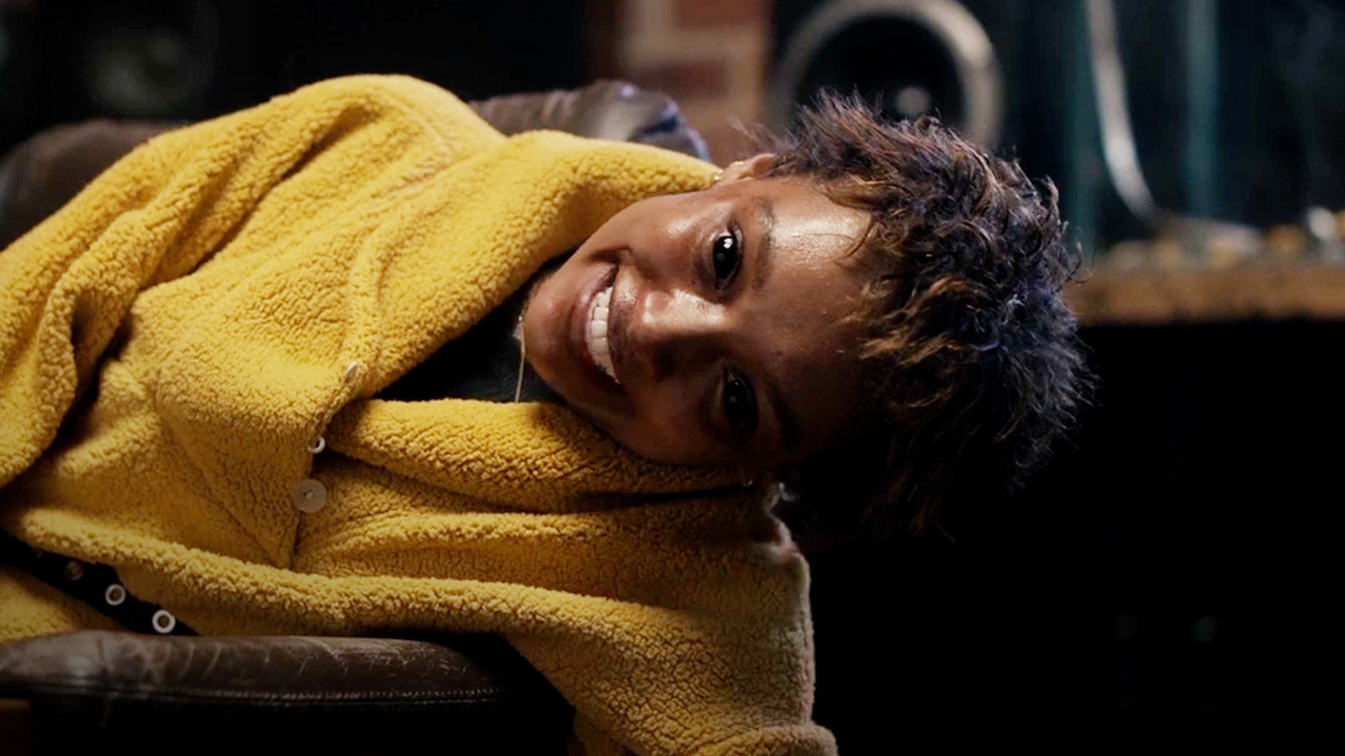 Person smiling, wearing a cozy textured wrap, seated comfortably in a relaxed setting