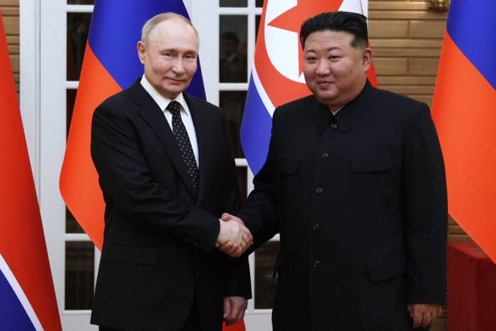 Two political leaders shaking hands in a formal setting with flags in the background