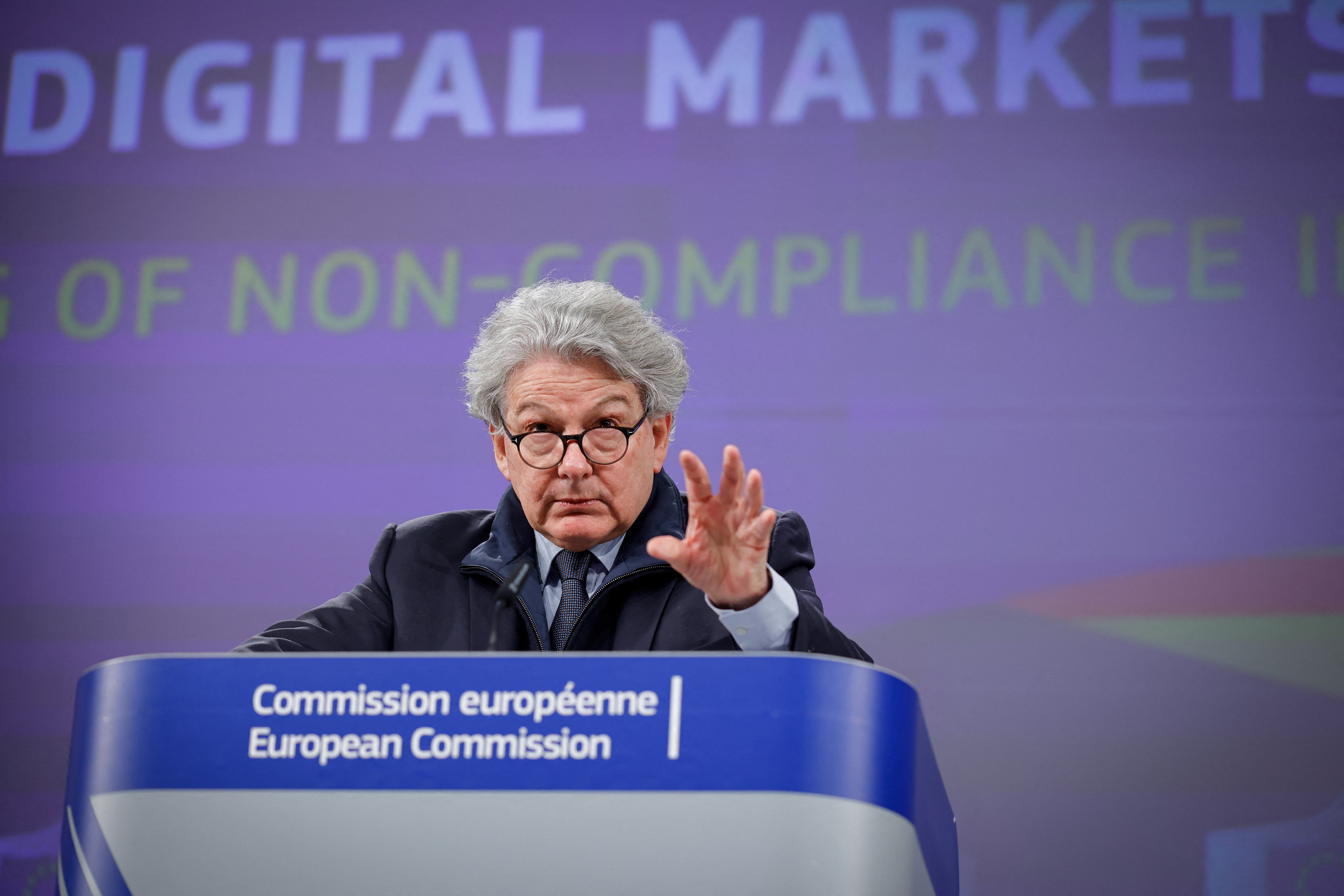 A person speaking at a podium labeled "European Commission" with "Digital Markets" text in the background