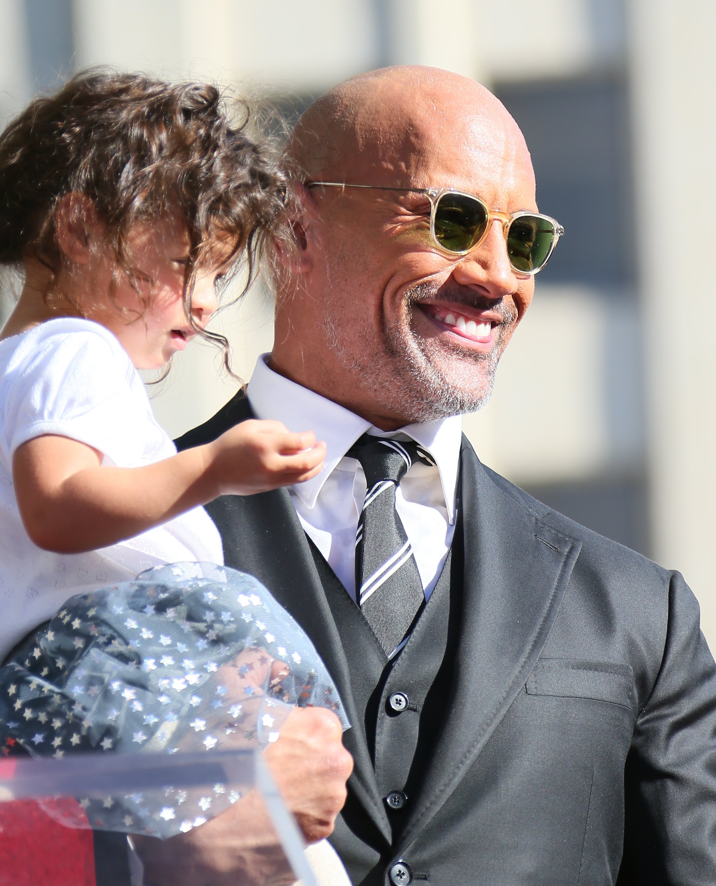 Dwayne Johnson in a suit and tie holding a child
