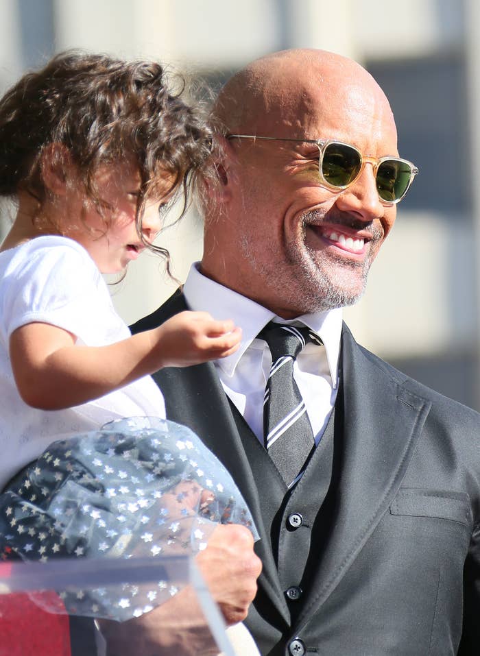 Dwayne Johnson in a suit and tie holding a child