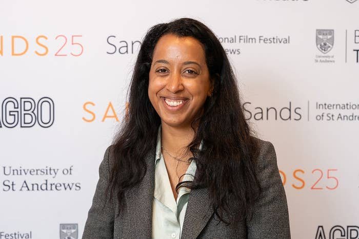 Person smiling at event backdrop with text related to Sands International Film Festival, wearing a blazer and shirt