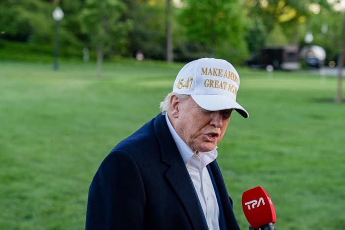 Person outdoors wearing a &quot;Make America Great Again&quot; hat, speaking into a microphone labeled &quot;TPA.&quot;