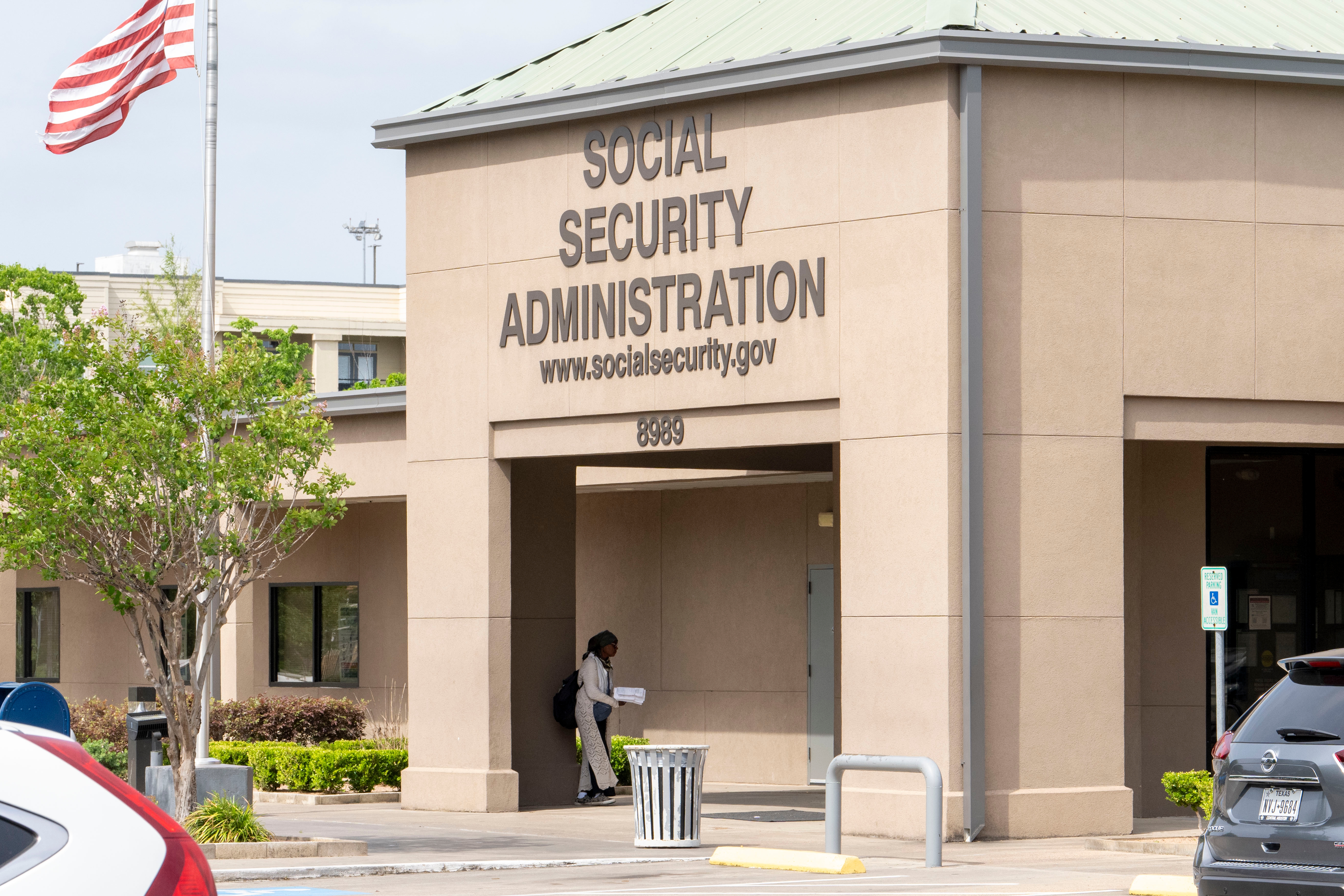 Exterior of Social Security Administration building with website address displayed, and a person entering through the doorway