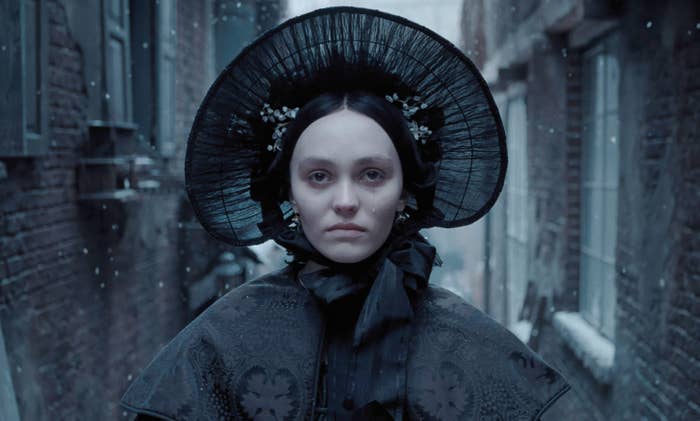 Person in vintage Victorian attire with a bonnet, standing in a narrow alley. Snowflakes visible in the air