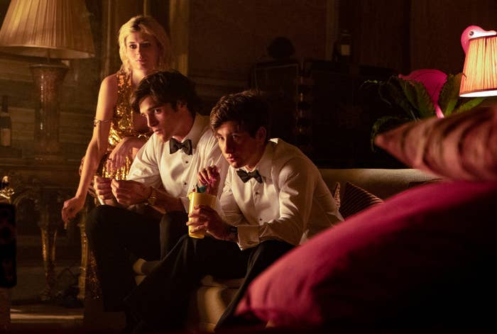 Three people in formal attire, two men in tuxedos and a woman in an elegant dress, are seated in a dimly lit, upscale setting