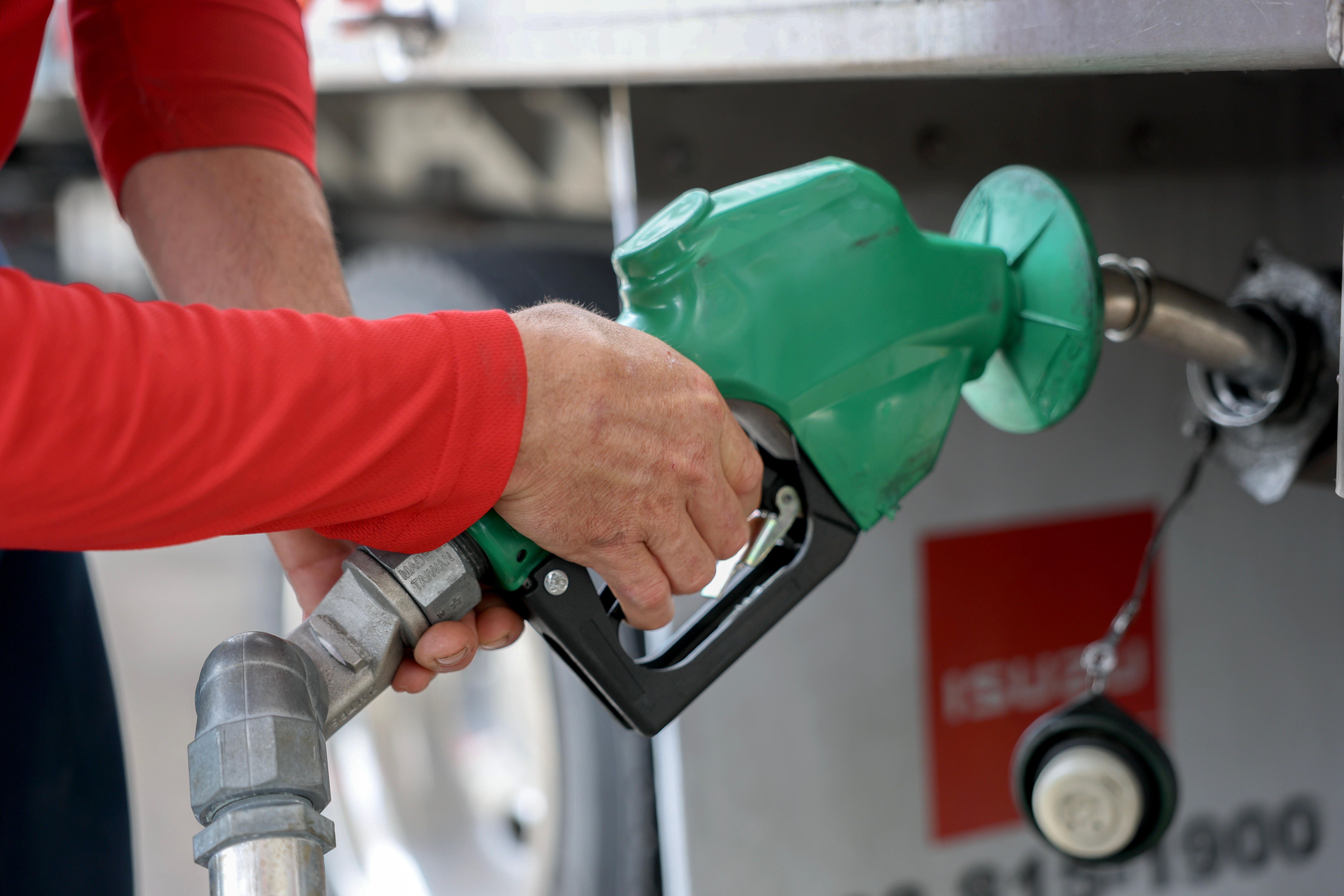 Person in a long-sleeve shirt refueling a vehicle at a gas pump, inserting a nozzle into the tank
