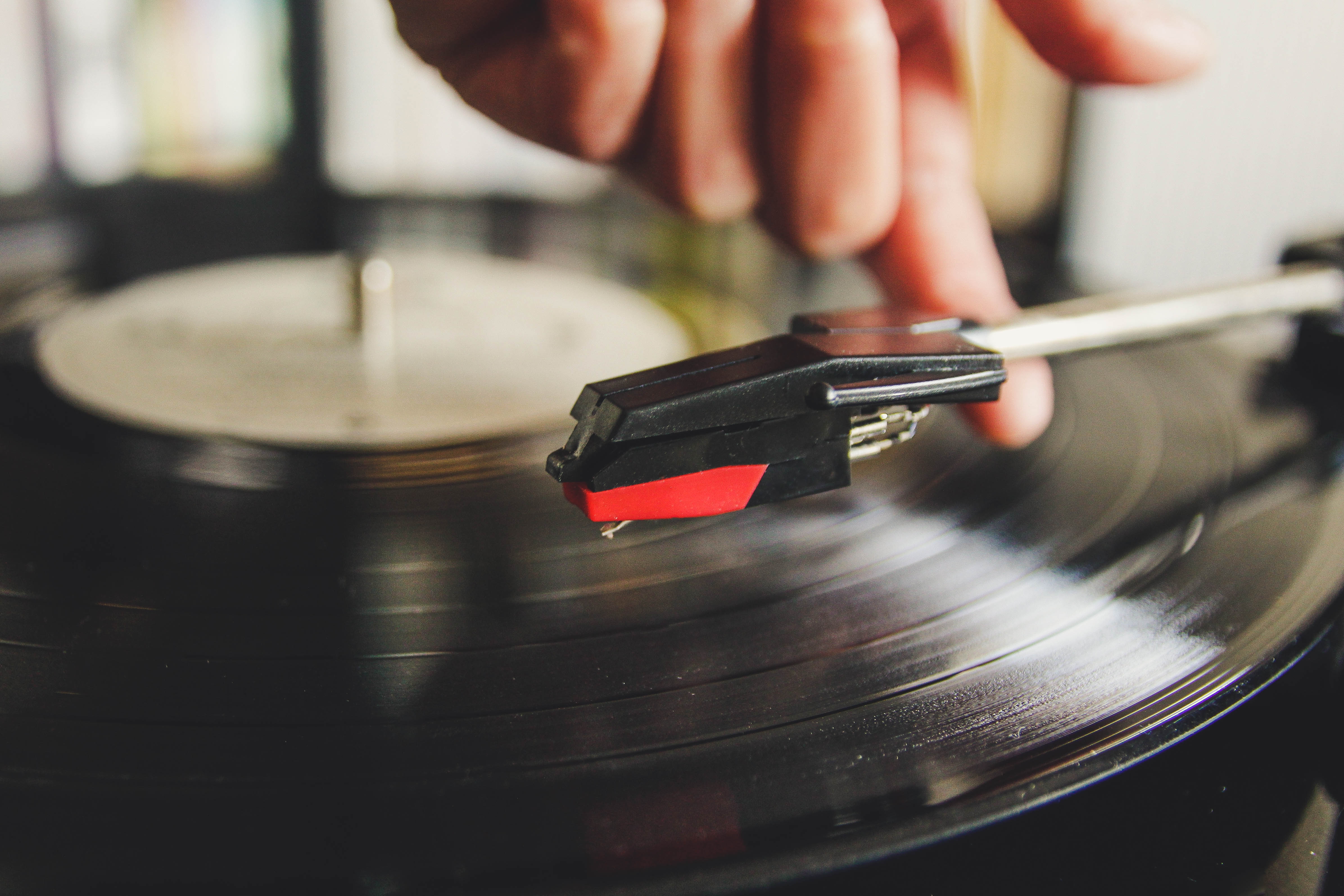 Hand gently places the needle on a spinning vinyl record on a turntable.