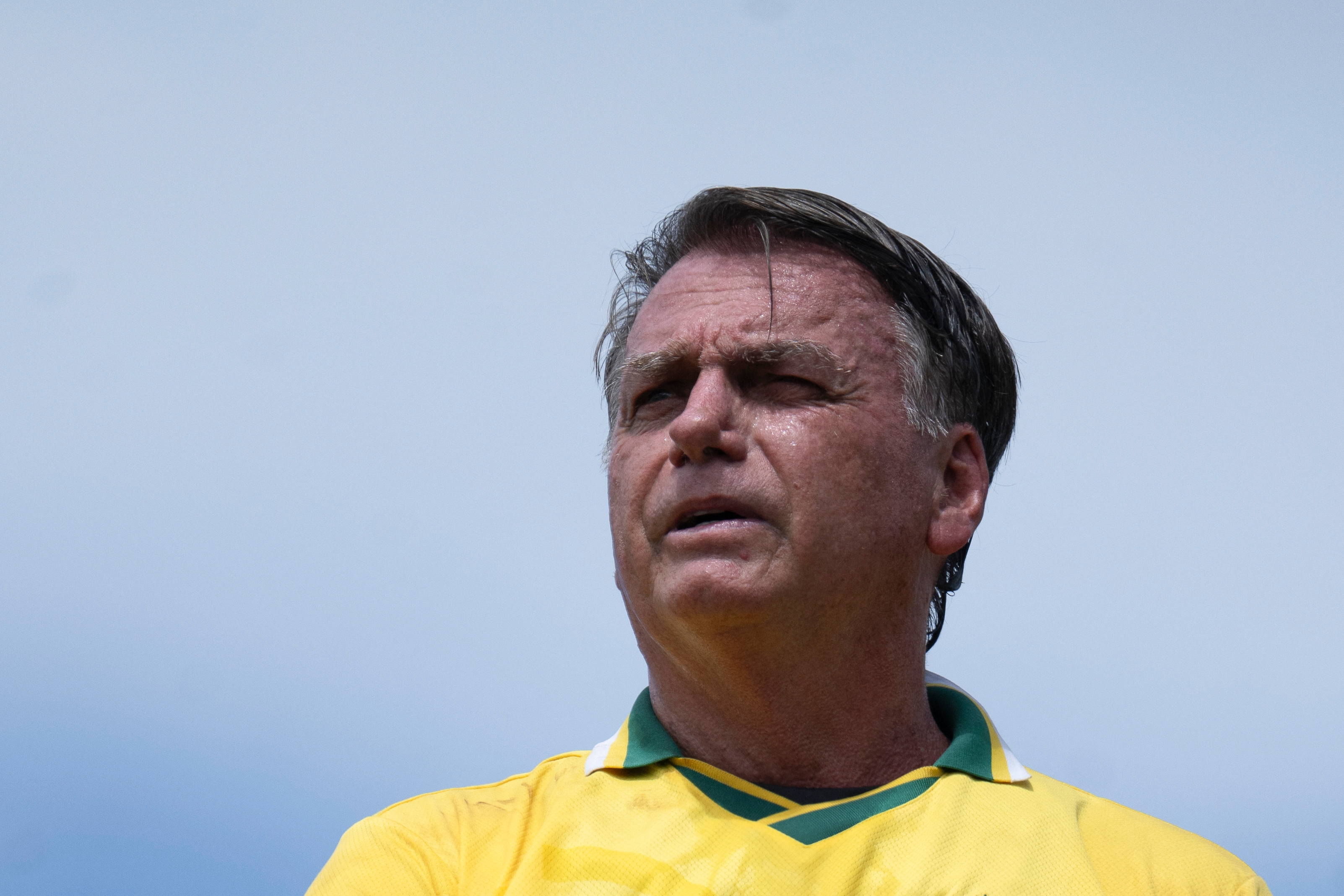 A person in a soccer jersey looks into the distance against a clear sky backdrop